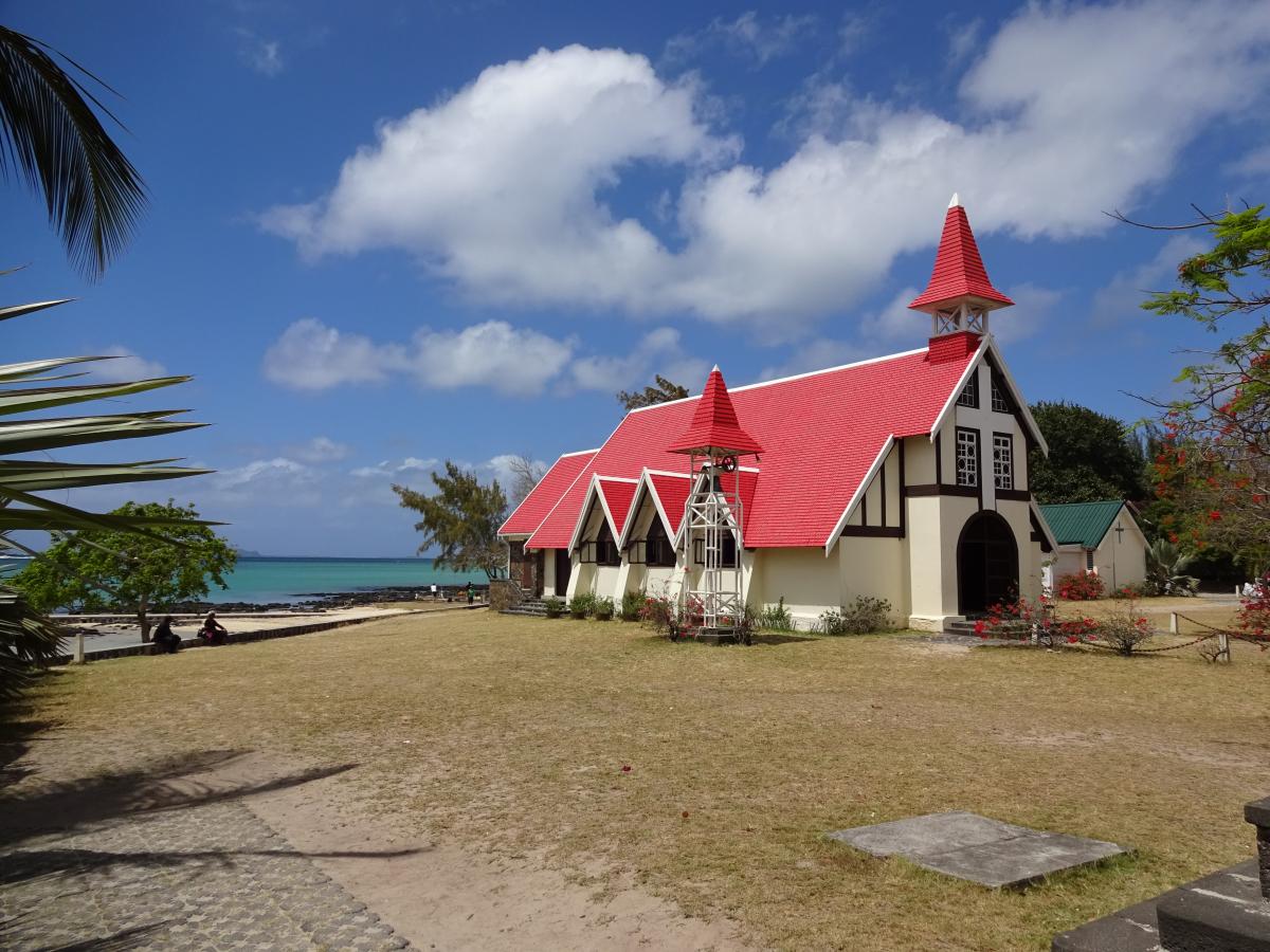weiße Kirche mit Rotem Dach zwischen Palmen am Strand von Mosambik mit Meer im Hintergrund und weißen Wolken am Blauen Himmel