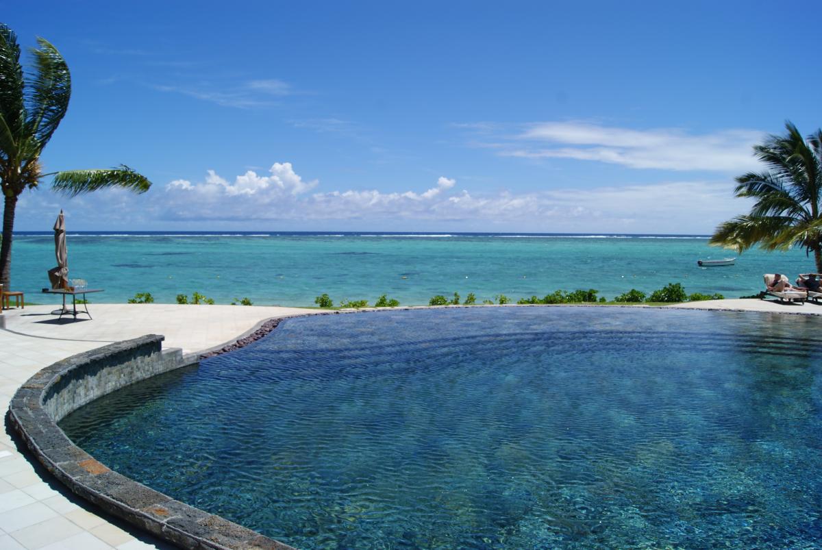 Infinity Pool mit Blick aufs Meer am Strand von Mosambik bei strahlend blauem Himmel und Sonnenschein, Palmen stehen an den Seiten des Pools